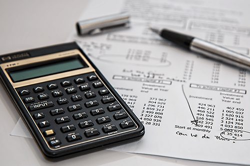 A calculator sitting next to a budget sheet with a pen
